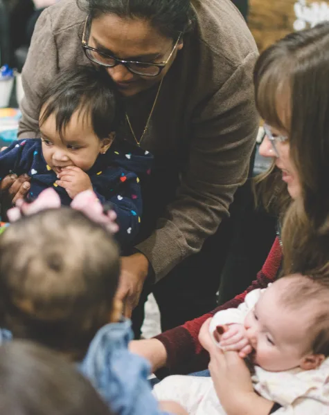 Volunteers and toddlers laughing and playing in a circle.